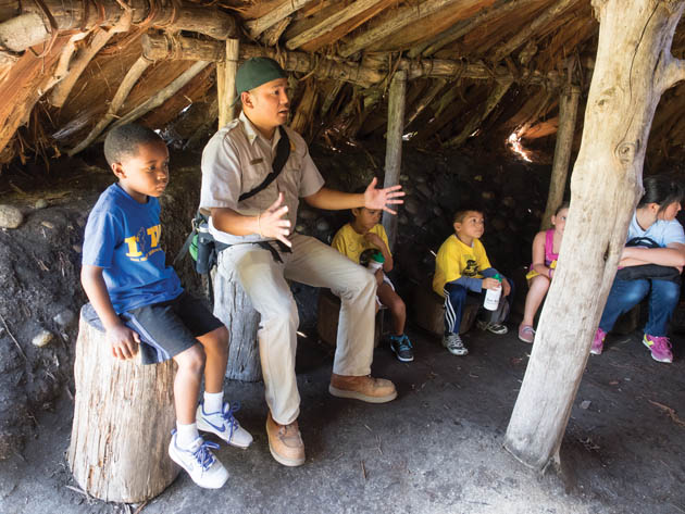 Inside a reconstructed traditional Ohlone dwelling, Naturalist Francis Mendoza talks with students from Union City Hillview Crest Elementary School about the people who once inhabited the area that is now Coyote Hills Regional Park in Fremont. (Photo by Scott Braley, scottbraley.com)