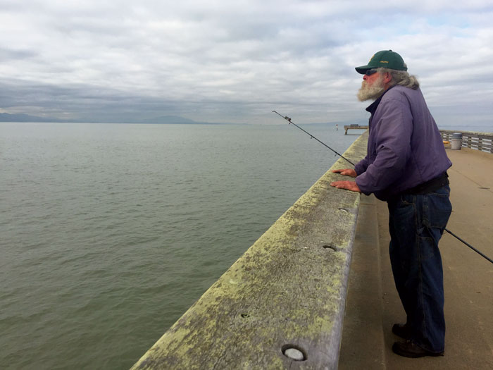 Fishing in the Bay since the 1950s, Curtis Reichert casts from the pier in Point Pinole Regional Shoreline park, hoping to hook a striped bass. (Photo by De Tran)