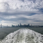 The wake of a ferry, photographed from the boat, with SF skyline in the distance