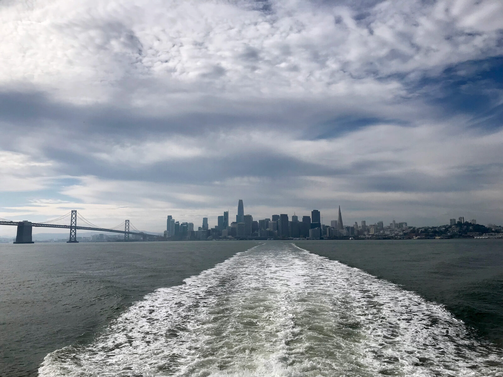 The wake of a ferry, photographed from the boat, with SF skyline in the distance